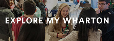 A group of people engaged in conversation in a room; overlaid text reads "Explore My Wharton."