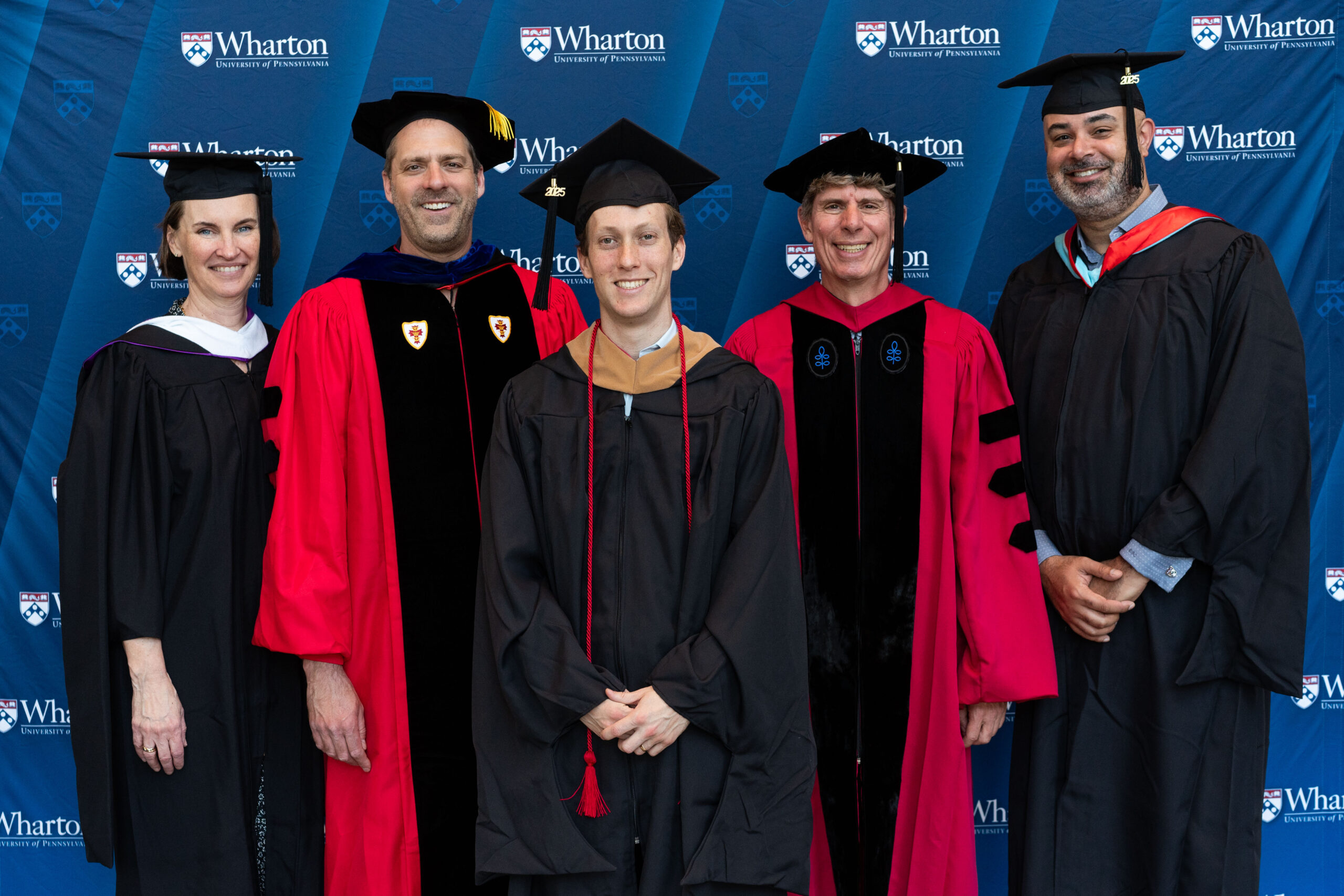 A small group of people in academic regalia posing for a graduation photo in front of a "Wharton University of Pennsylvania" backdrop.